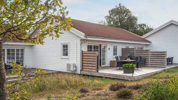 A single-story house with a patio area, a barbecue grill, and a seating arrangement.