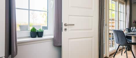An open door leading to a dining area with a table set for two, a window with curtains, and a radiator below.