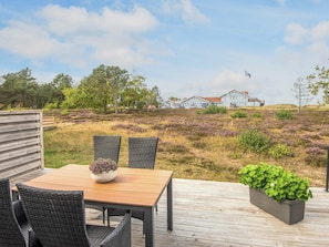 A wooden deck with a table and chairs, a potted plant, and a view of a house in the background. - 4 Star Holiday Home in Laeso (Læsø)