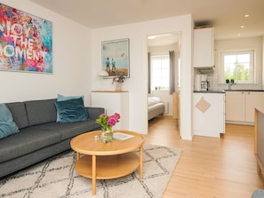 A modern living room with a sofa, coffee table, and artwork. A hallway leads to a bedroom and a kitchen. - 4 Star Holiday Home in Laeso (Læsø)