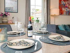 Mesa de jantar posta com pratos, talheres e copos de vinho, com uma garrafa de vinho ao centro.