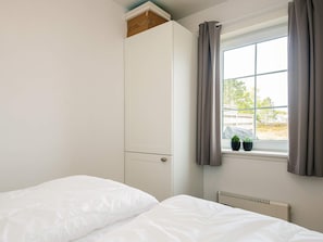 Un dormitorio con una cama, un armario, una ventana con cortinas y un radiador.