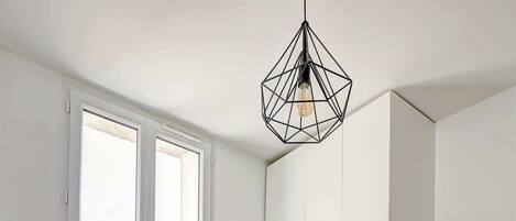 A neatly made bed with a tray of croissants and orange juice, a white wardrobe, and a geometric pendant light.