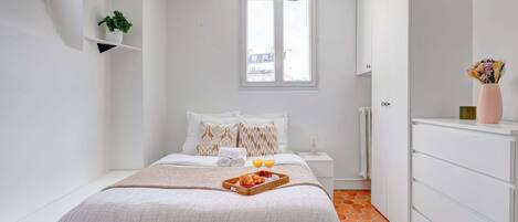 Ein Schlafzimmer mit Bett, Nachttisch und Fenster. Auf dem Bett steht ein Tablett mit Croissants und Saft.