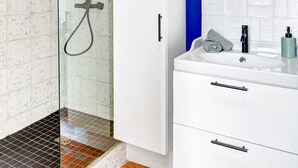 A bathroom with a glass-enclosed shower, white cabinets, a round mirror, and a tiled floor.