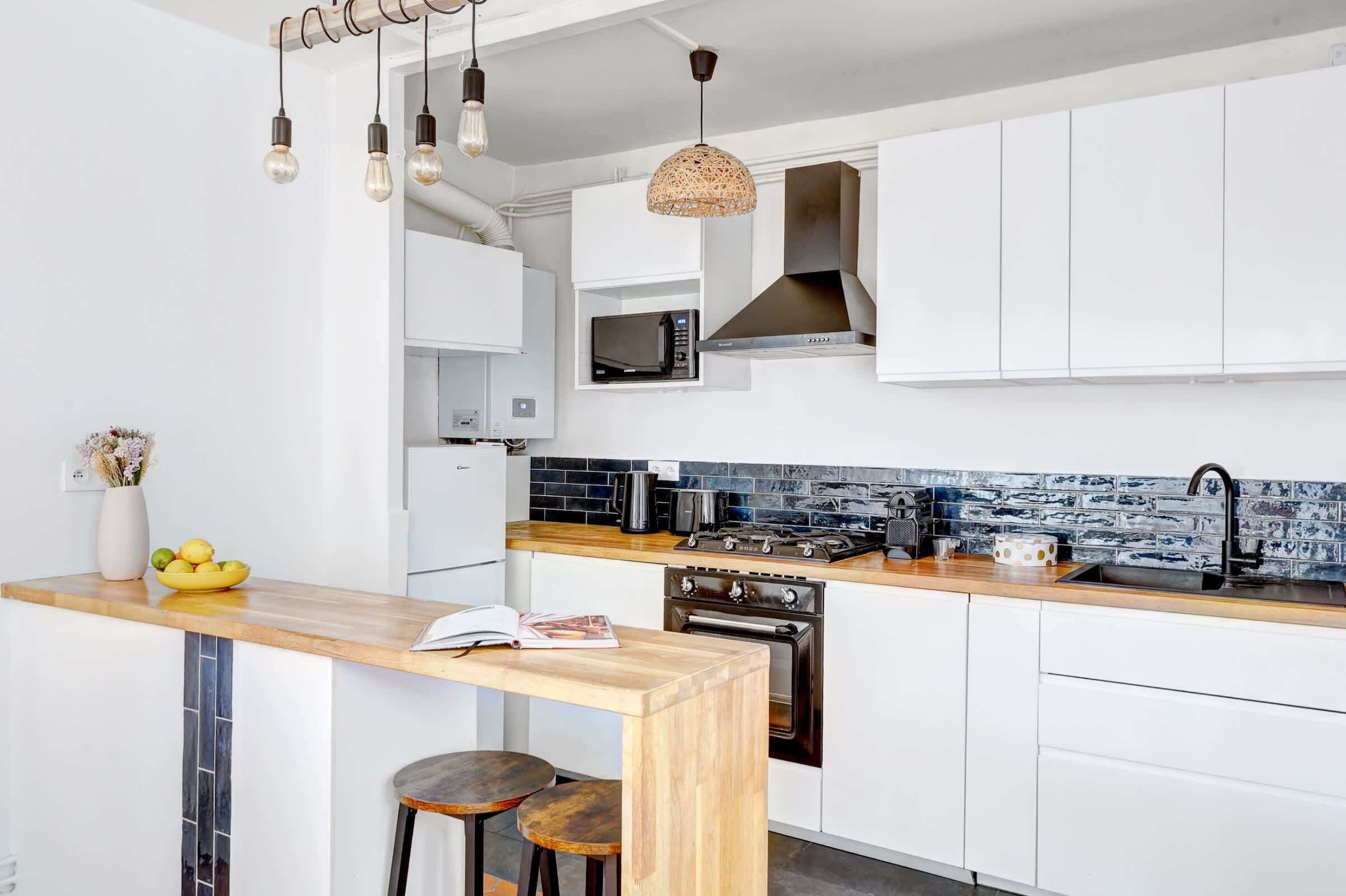 Une cuisine moderne avec des armoires blanches, un plan de travail en bois, un four à micro-ondes encastré, une cuisinière et un luminaire suspendu.