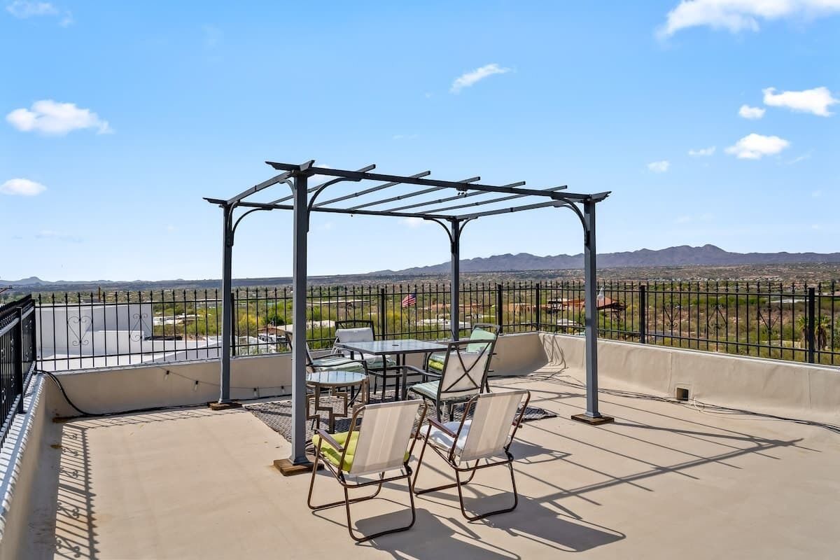 A rooftop patio with outdoor seating and a pergola, overlooking a desert landscape.