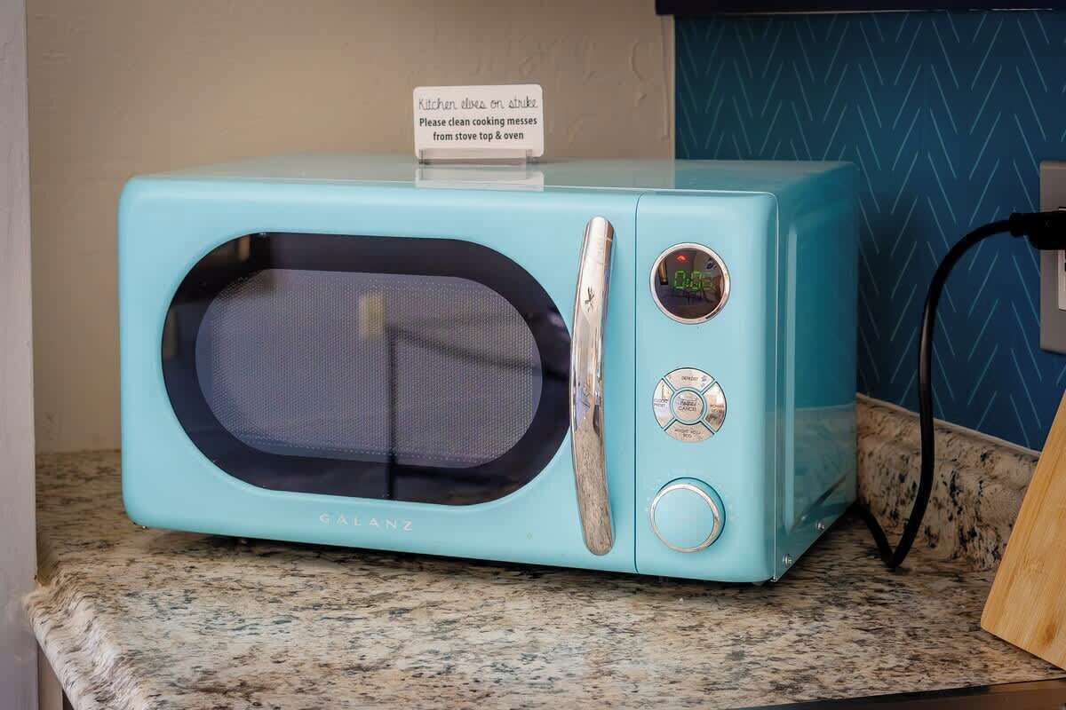 Un four à micro-ondes de couleur turquoise, doté d’un écran numérique et d’un panneau de commande, posé sur un plan de travail en granit.