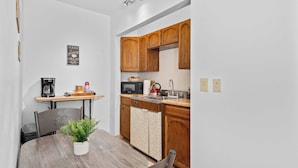 Cocina compacta con armarios de madera, microondas, tetera y una pequeña mesa de comedor con planta en maceta.