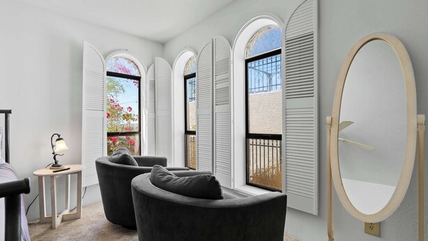 Una habitación moderna con un ventanal grande, dos sillones negros, una mesita con lámpara y un espejo grande en la pared.