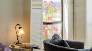 Una habitación con una cama, una silla, una mesa con una lámpara y una ventana con contraventanas.