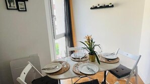 Een eetgedeelte met een ronde tafel voor vier personen, witte stoelen, een kleine potplant en een plank met decoratieve objecten.