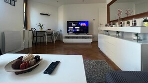 Een moderne woonkamer met een flatscreen televisie, een eethoek en een witte console tafel.