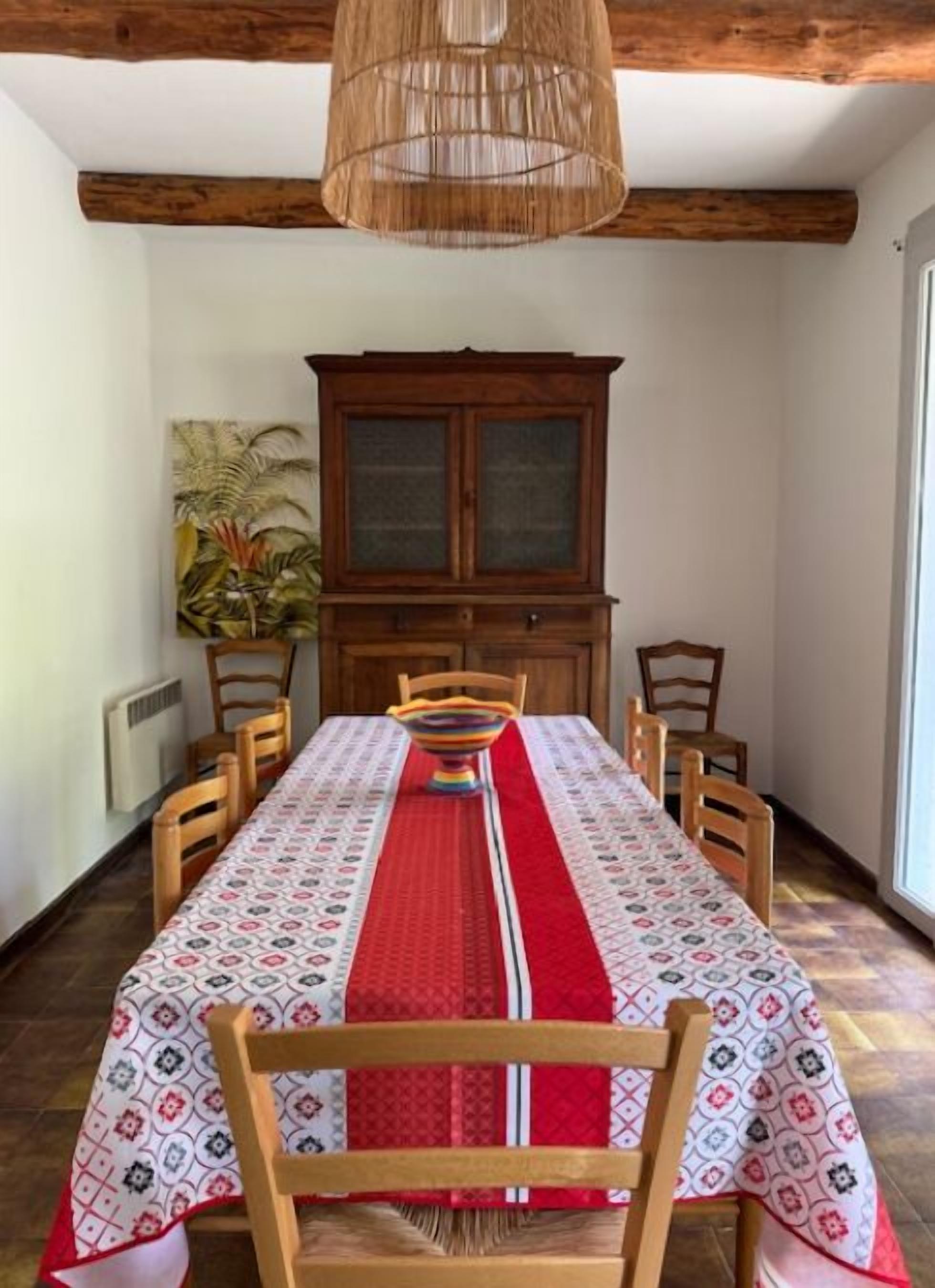 A dining room with a long table, wooden chairs, a cabinet, and a hanging light fixture.