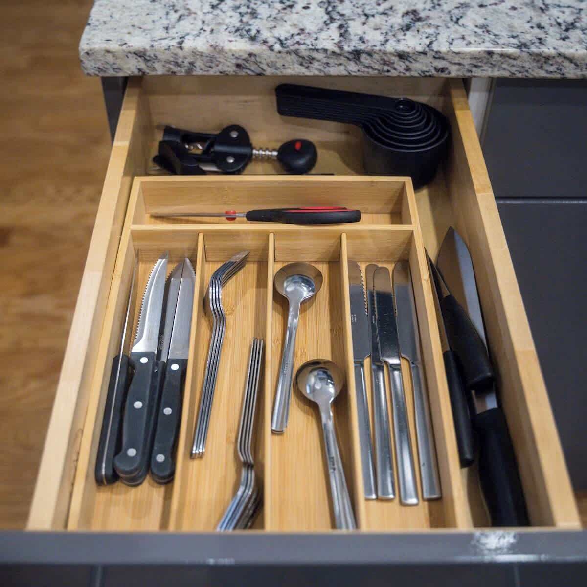 A drawer with neatly organized kitchen utensils including knives, forks, spoons, and a can opener.
