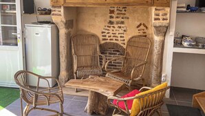 Ein Zimmer mit einem rustikalen Kamin aus Ziegeln, Korbstühlen, einem Holztisch und einem weißen Kühlschrank.