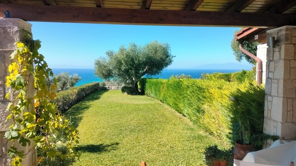 A well-maintained garden with a view of the sea, stone walls, and a pergola structure.