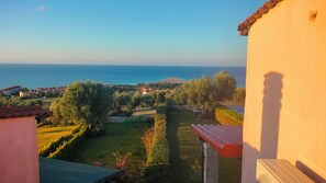 Enjoy a serene coastal view from this balcony overlooking a lush garden and the distant sea.