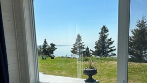 Ett rum med ett stort fönster som vetter ut mot en gräsyta med träd och en vattenyta.
