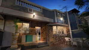 Un edificio de dos pisos con fachada de piedra, un balcón con barandilla y una pequeña zona exterior con mesa y sillas.