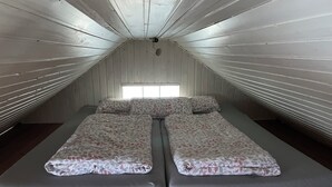 A room with a sloped ceiling and wooden walls, featuring a bed with a floral bedspread and two pillows.