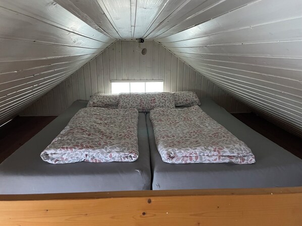 Een kamer met een schuine plafond en houten wanden, met een bed met een bloemenbedekking en twee kussens.