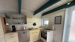 A compact kitchen with a dishwasher, stove, and sink. There is a window with a plant, and a door leading outside.