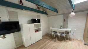 A room with a white cabinet, a flat-screen TV, a table with chairs, and a ceiling fan.