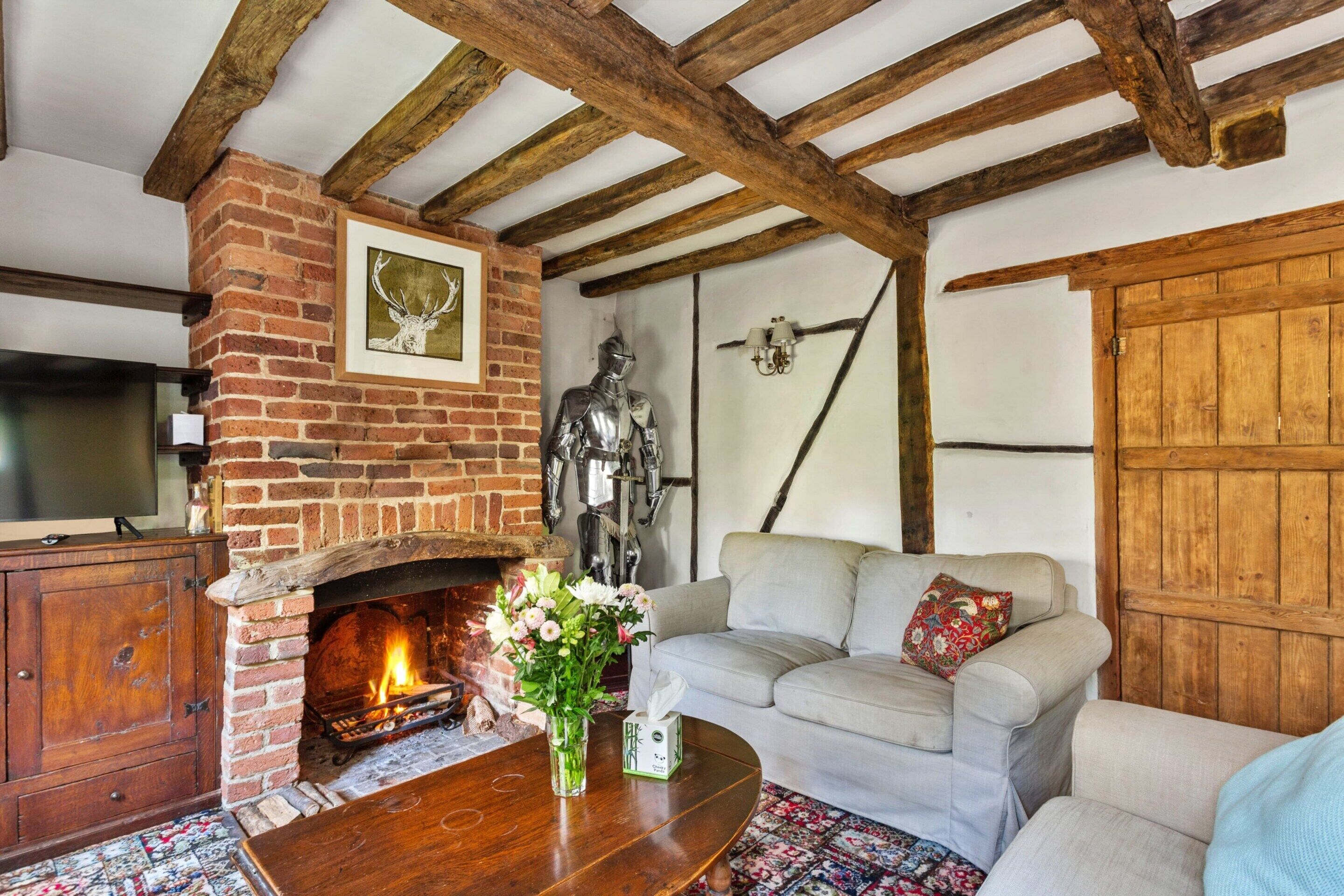 A rustic living room with exposed wooden beams, a brick fireplace, a statue, and a sofa with cushions.