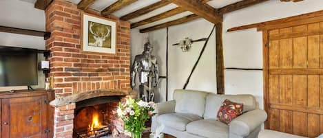 A rustic living room with exposed wooden beams, a brick fireplace, a statue, and a sofa with cushions.