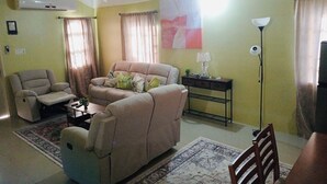Un salon avec un canapé beige, un fauteuil inclinable, une petite table avec une lampe et un grand tableau accroché au mur.