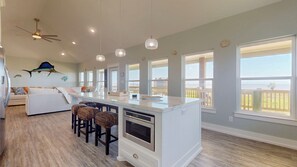 A modern kitchen with a central island, bar stools, and large windows offering views of the ocean. - Captain Sparrows Parley (Bolivar Peninsula)