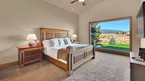 A bedroom with a large window, a bed, a nightstand, a lamp, and a ceiling fan. - Ski & Golf Retreat w/ Stunning Mountain Views (Eden)