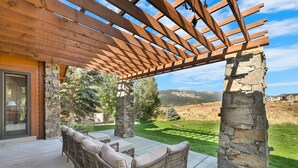 A covered patio with wicker furniture and stone pillars. - Ski & Golf Retreat w/ Stunning Mountain Views (Eden)