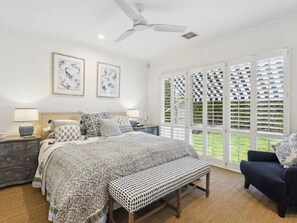 Une chambre à coucher comprenant un lit, des tables de chevet, un banc, une chaise et un ventilateur de plafond.