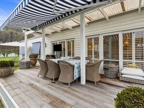 A covered outdoor patio with a table and chairs, surrounded by potted plants and wicker furniture.