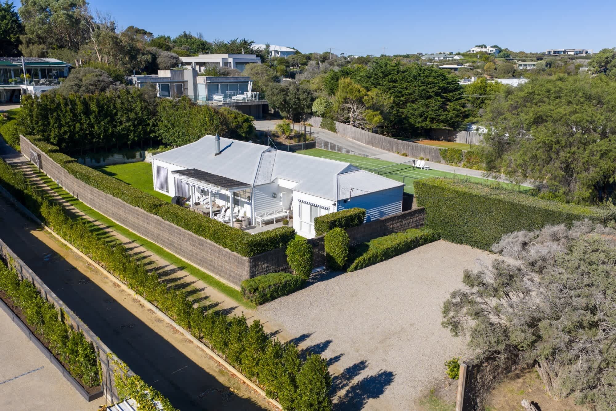 A modern house with a large patio, surrounded by well-maintained hedges and trees.