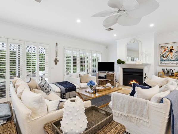 A spacious living room with a fireplace, a television, and a ceiling fan.