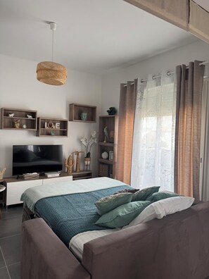 Une chambre moderne avec un lit, une télévision, des étagères en bois et une grande fenêtre avec des rideaux.