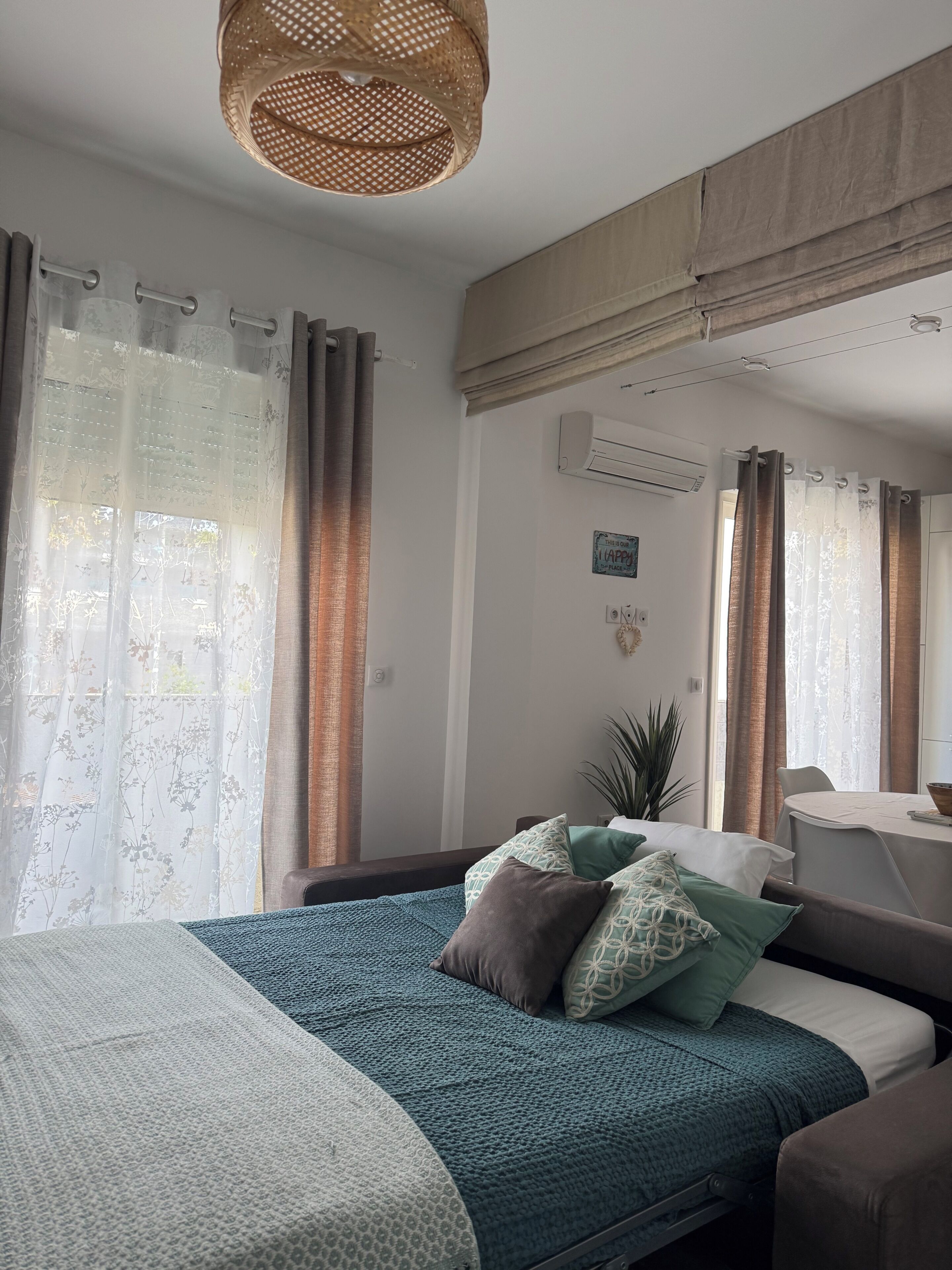 A bedroom with a bed, curtains, an air conditioning unit, a mirror, and a small table with a bowl.