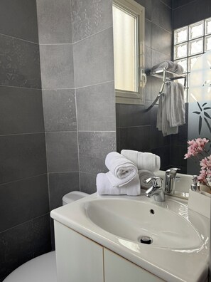 Une salle de bain avec des murs recouverts de carreaux foncés, un lavabo blanc, un miroir et un porte-serviettes.