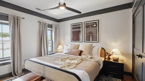 Ein Schlafzimmer mit Bett, Nachttischen, Deckenventilator und einem Fenster mit Vorhängen.