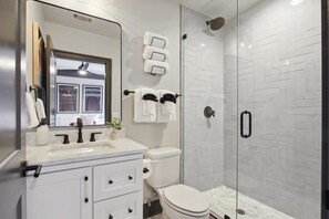 Een moderne badkamer met een douchecabine van glas, een wit wastafelmeubel met een marmeren blad en een toilet.