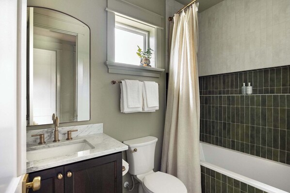 Un baño con lavamanos de mármol, inodoro, ventana con planta y cortina de ducha.