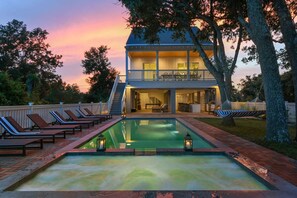 Una casa de dos pisos con piscina, sillas de descanso y una hamaca.