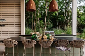 Un espace extérieur aménagé pour les repas, avec des chaises en osier, un barbecue et des lampes en osier suspendues.