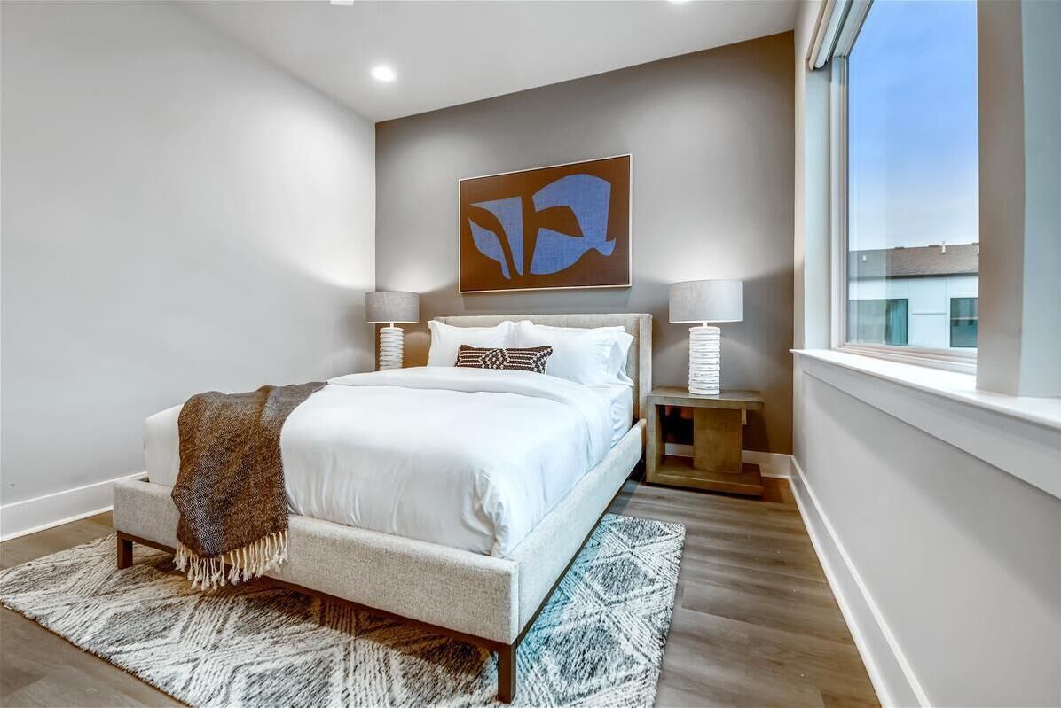 Une chambre à coucher moderne avec un grand lit, des lampes de chevet, un plaid et une œuvre d’art géométrique accrochée au mur.