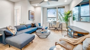 Un salon moderne avec un canapé d’angle, une table basse, un meuble pour la télévision et un ventilateur de plafond.