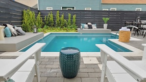 Une piscine rectangulaire avec des chaises longues blanches et un tabouret rond à la texture particulière.