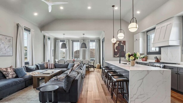 Une cuisine moderne dotée d’un îlot en marbre, un coin repas avec une longue table et des chaises, et un salon avec un canapé et une table basse.